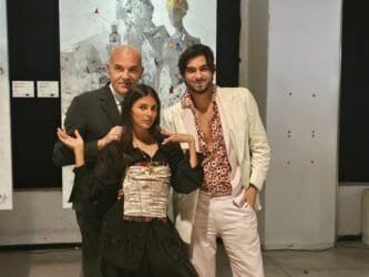 Tre persone sorridenti in abiti eleganti davanti a quadro