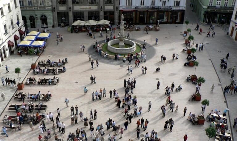 Piazza affollata con fontana centrale e tavolini