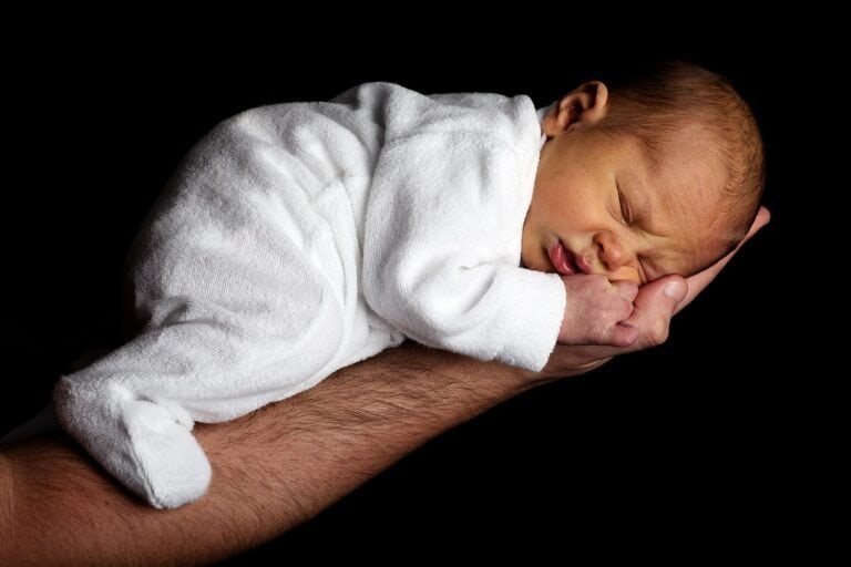 Neonato addormentato su braccio adulto, sfondo nero