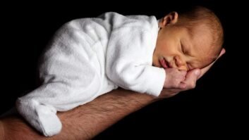 Neonato addormentato su braccio adulto, sfondo nero