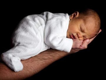 Neonato addormentato su braccio adulto, sfondo nero