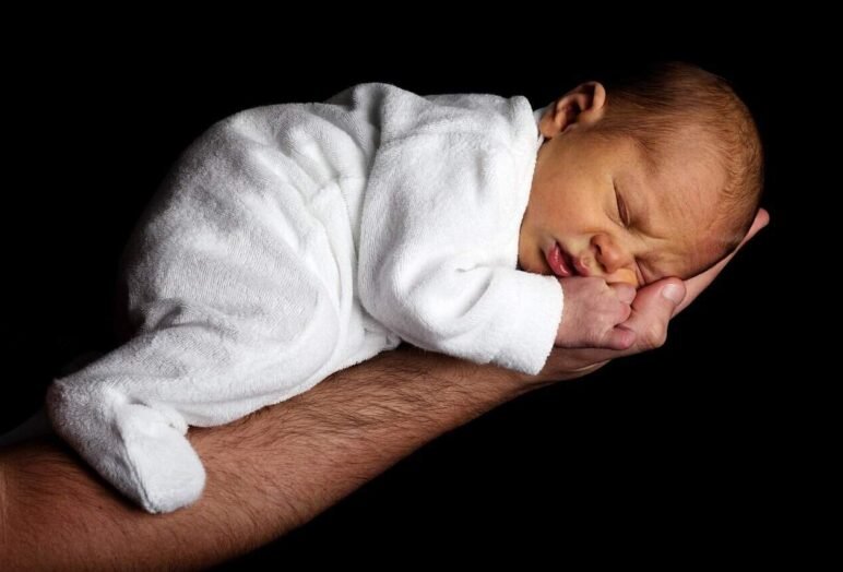 Neonato addormentato su braccio adulto, sfondo nero