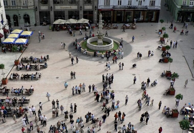Piazza affollata con fontana centrale e tavolini