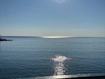 Sole riflette sul mare con ringhiera in primo piano