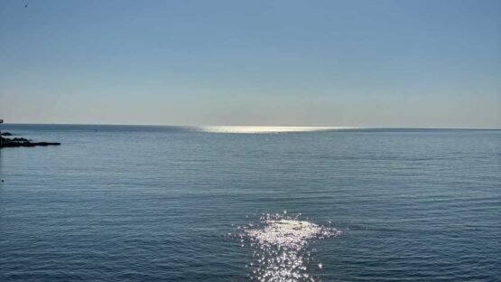 Sole riflette sul mare con ringhiera in primo piano